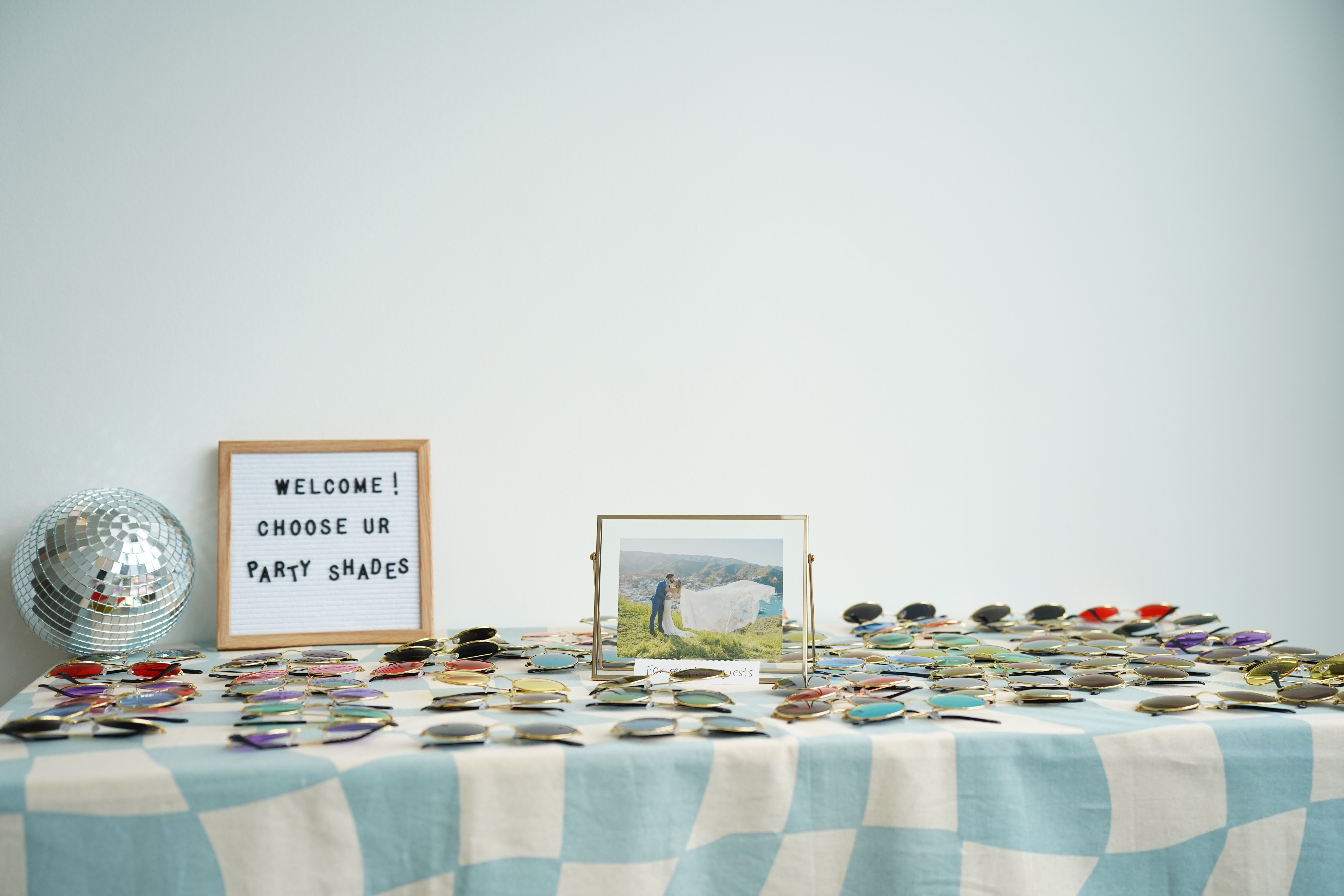 Sunglasses table with letterboard reading Welcome! Choose ur party shades